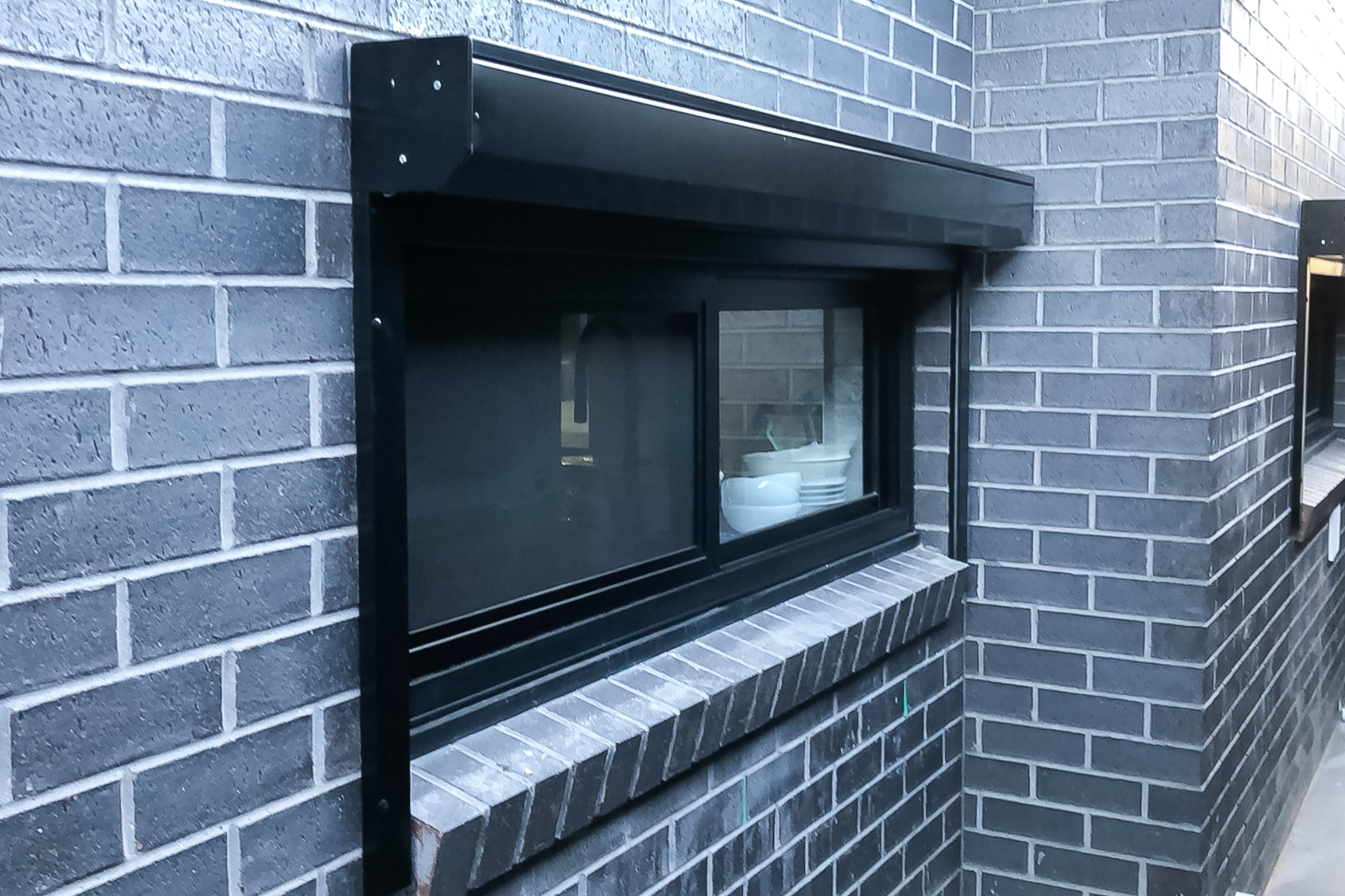 In this image, the roller shutters offered by Unique Blinds are shown on the external of the house. The black framing of the roller shutters nicely follows the grey brick colour scheme.