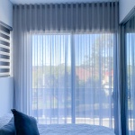 Sheer curtains displayed in a bedroom following a neutral colour scheme. This project for inspiration was completed by Unique Blinds in a Sydney-based home to showcase the grey sheer curtains' ability to softly diffuse light.