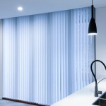 Vertical blinds that are white coloured are displayed within a kitchen focused living area to nicely tie together the clients living space.