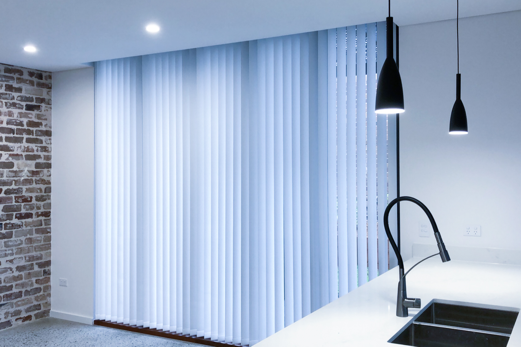 Vertical blinds that are white coloured are displayed within a kitchen focused living area to nicely tie together the clients living space.