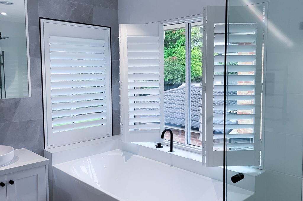 Plantation shutters are shown in a neutral colour scheme for a bathroom in a Sydney home. This type of window covering provides the ability to reduce the lighting in a room gradually.