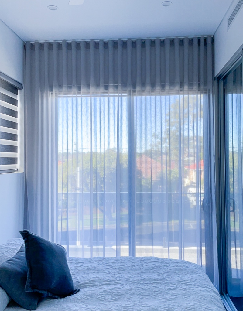 Sheer Curtains Vertical Sheer curtains displayed in a bedroom following a neutral colour scheme. This project for inspiration was completed by Unique Blinds in a Sydney-based home to showcase the grey sheer curtains' ability to softly diffuse light.